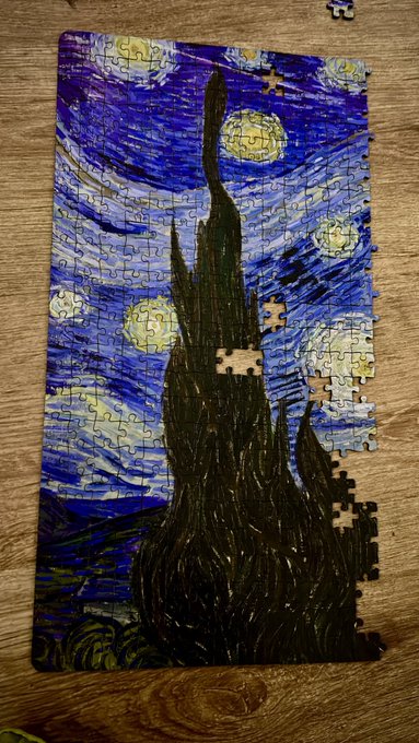 A partially completed jigsaw puzzle of Vincent van Gogh's 'Starry Night' rests on a wooden floor, with about a dozen pieces still missing from the right edge.