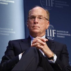 A man in a dark suit and glasses sits thoughtfully with his hands clasped, photographed against a backdrop displaying the 'IIF' logo, suggesting an Institute of International Finance event.