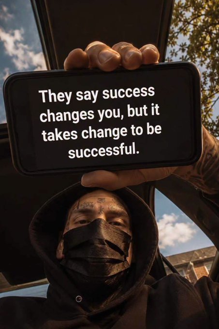 A person in a black hoodie and face mask holds up a phone displaying the quote 'They say success changes you, but it takes change to be successful.'