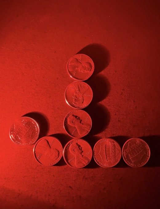 A collection of seven copper-colored coins arranged in a small triangular pattern on a dark red surface, illuminated by warm light.