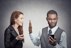 A stock photo showing a smiling woman giving a high-five to a man who is looking at his smartphone with a displeased expression.