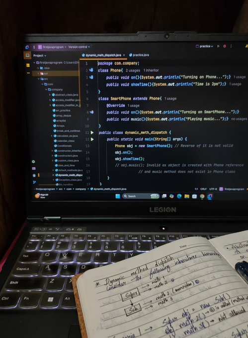 A laptop screen displays Java code demonstrating dynamic method dispatch with Phone and SmartPhone classes, while a handwritten notebook below illustrates related concepts like inheritance hierarchies and method overrides, suggesting the user is taking physical notes while learning object-oriented programming.