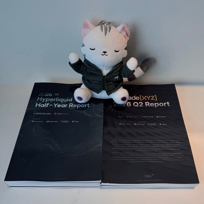 A small white plush cat toy wearing a black jacket sits on top of two reports: '2026 H1 Hyperliquid Half-Year Report' and 'Stride[XYZ] 2026 Q2 Report'.