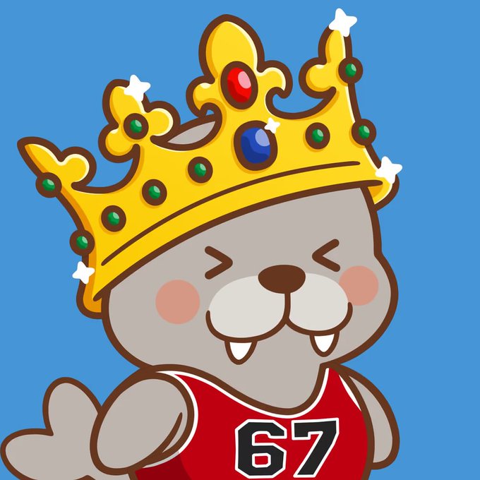 A cute cartoon gray seal mascot wearing a jeweled gold crown and a red jersey with the number "67" beams with pride against a blue background, fitting the celebratory NFT reveal announcement from WagyuBrands showcasing new artwork.
