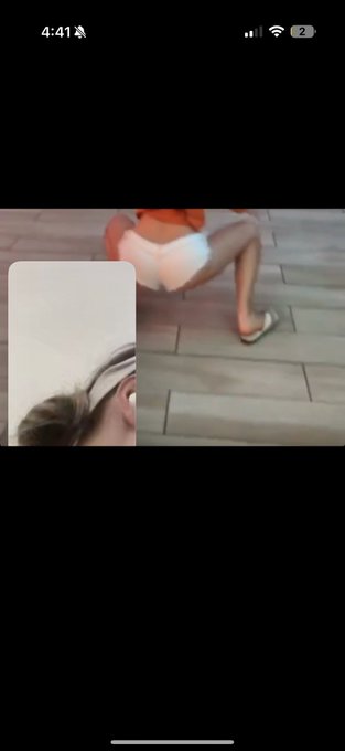 A mobile video call screenshot showing a person sitting on wooden decking wearing white shorts and flip-flops, with a smaller picture-in-picture view of another person wearing a visor.