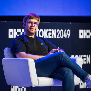 A bearded man with glasses sits relaxed in a white armchair on stage at TOKEN2049, likely Wintermute CEO Evgeny Gaevoy discussing his firm's new US broker-dealer registration. The "$3.5 TRILLION" crypto trading firm is now positioned to compete with traditional market makers like Jane Street and Citadel Securities in crypto ETF trading.