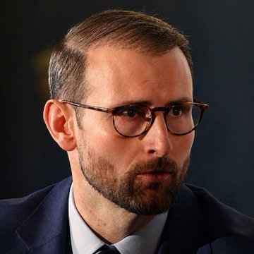 A man with glasses, a beard, and dark suit appears serious while speaking, in what looks like a formal hearing or press setting. His image accompanies a post about White House crypto adviser Patrick Witt expressing the administration's commitment to passing the CLARITY Act, though the person pictured cannot be definitively identified from the image alone.