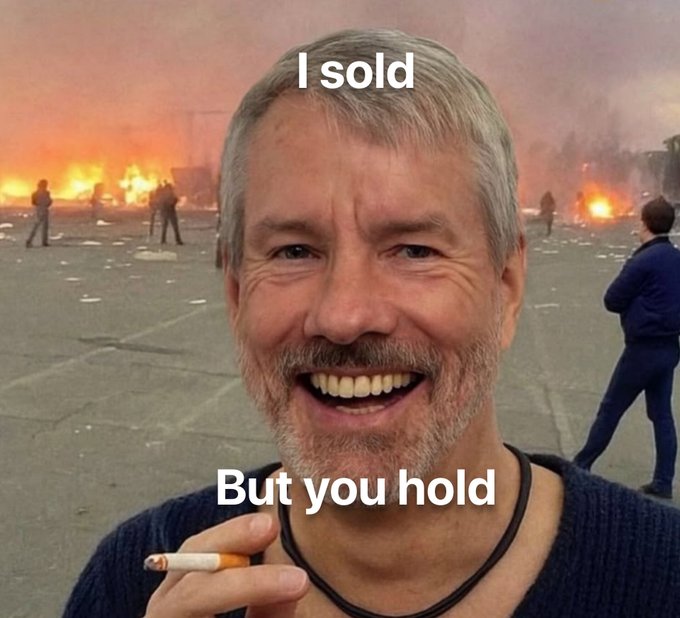A meme shows a grinning man holding a cigarette in front of a fiery, chaotic background, with text reading "I sold" above and "But you hold" below—mocking Michael Saylor's Strategy selling 1,637 Bitcoin worth $102 million while continuing to advocate for others to hold.