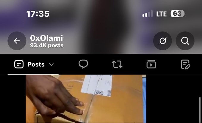 A mobile screenshot of the X (Twitter) profile '0xOlami' with 93.4K posts, showing a video of a hand handling a package with a shipping label.