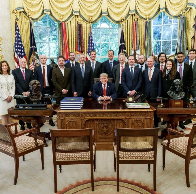 A group photo taken in the Oval Office, featuring President Donald Trump seated at the Resolute Desk surrounded by approximately fifteen individuals in formal attire, with American and military flags and bronze busts visible in the background. The post appears to highlight one of the men standing in the group, identified as "Bradly," connecting him to Ripple CEO Brad Garlinghouse in a formal White House setting.
