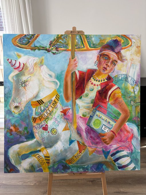 A vibrant, colorful painting on an easel depicting a person riding a white unicorn-like horse, featuring text elements like 'CIRCUS', 'JOY', and 'PEACE' woven into the design.