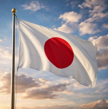The Japanese flag waves against a blue sky with scattered clouds during golden hour lighting.