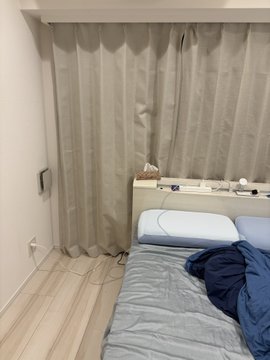 A cozy bedroom in a small Tokyo rental with beige curtains and a neatly made bed is shown as the speaker's new "little nest." The post thanks @bcgame for sponsoring the rent, highlighting the modest but personal space they've just moved into.