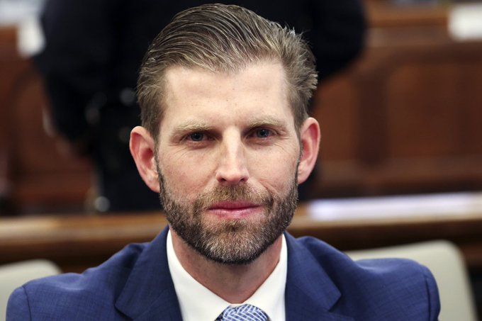 A man with a neatly groomed beard and styled brown hair, wearing a navy blue suit, white shirt, and blue patterned tie, sits in what appears to be a formal government or hearing chamber setting. The image appears unrelated to the post's content about Eric Trump's comments on gold-to-Bitcoin capital rotation, as no identifying text, logos, or contextual clues connect the man pictured to that specific statement.