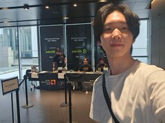 A man takes a selfie inside the 4th-floor entrance of the Japan Blockchain Week (JBW) event, with "Top Lee," founder of Bitmain and Ethereum maxi, visible in the background behind stanchions, though the long line prevented a closer conversation.