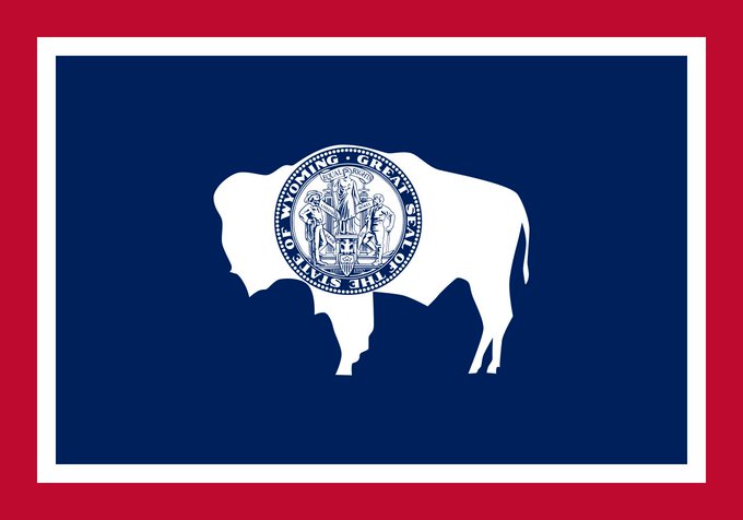 The image shows the Wyoming state flag, featuring a white bison silhouette on a navy blue field with the state seal in the center and a red border. It visually represents Wyoming, the state mentioned in the post for selecting Chainlink CCIP as the exclusive cross-chain infrastructure for its state-backed stablecoin.