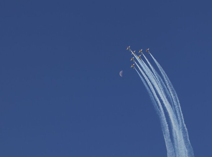 A formation of jets climbs across a deep blue sky, leaving sweeping white smoke trails beneath a faint crescent moon, matching the post’s love of the sky.