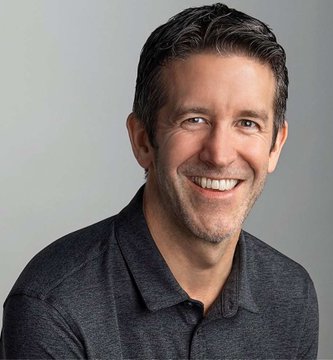 A headshot portrait of a smiling middle-aged man with short brown hair wearing a dark gray polo shirt against a plain gray background.
