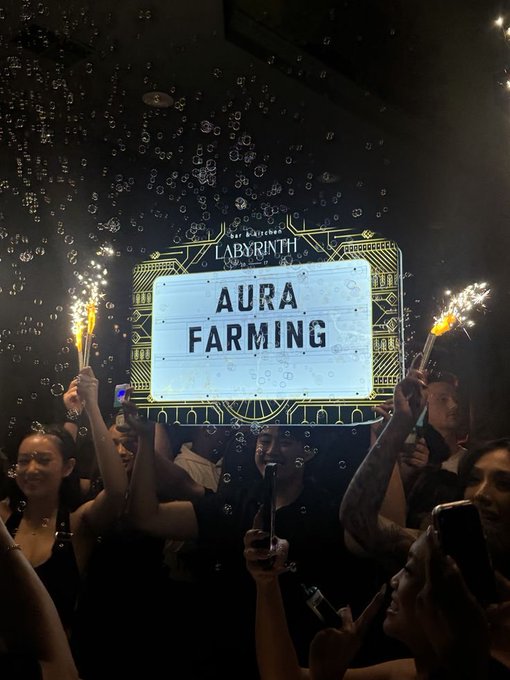 A nighttime club or concert scene where a crowd cheers and holds up sparklers beneath a brightly lit sign reading 'LABYRINTH' and 'AURA FARMING,' with bubbles floating in the air.
