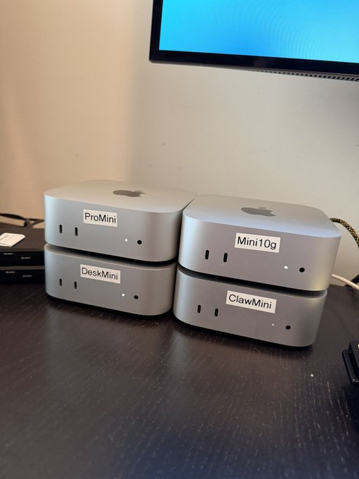 Four silver Apple Mac Mini computers stacked in two pairs on a desk, labeled with stickers reading 'ProMini', 'DeskMini', 'Mini10g', and 'ClawMini'.