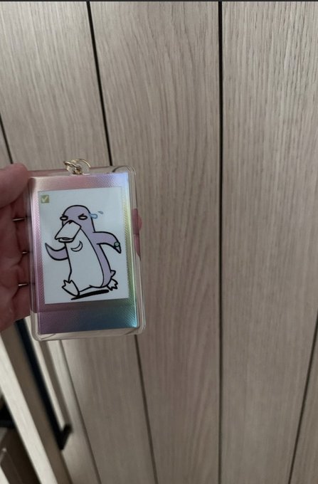 The image features a person holding up a keychain with a cartoon penguin design, which has a pink body and black beak. The text "gm BEAR-lin" can also be seen in the image. This suggests that the keychain is likely related to an event or gathering involving bears, possibly a themed party or a special occasion where attendees are encouraged to wear bear-themed accessories like this penguin keychain.