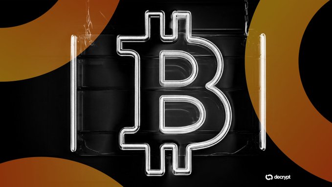 A white neon Bitcoin symbol glowing against a black and orange background with the 'decrypt' logo in the corner.