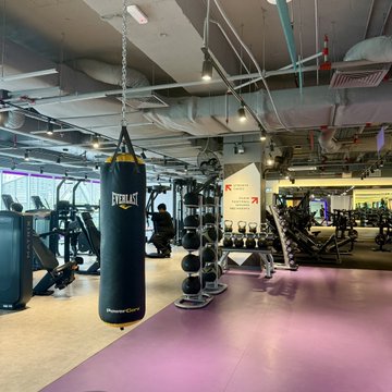 A photograph of a gym interior showing a black punching bag branded 'EVERLAST' hanging from the ceiling, surrounded by weight racks and exercise equipment.