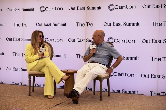 Former CFTC Chairman Chris Giancarlo speaks at the Out East Summit with Canton, holding a microphone while seated across from an interviewer in a yellow pantsuit.