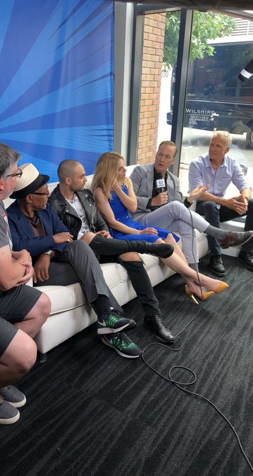 A group of people, including actors from "Suicide Squad" (Will Smith, Margot Robbie, and others), sit together on a white couch during a press interview at San Diego Comic-Con (SDCC), with one man holding a microphone and engaging them in conversation. The casual setting and panel-style seating align with the post's reference to "One time at SDCC," capturing a behind-the-scenes promotional moment from the event.