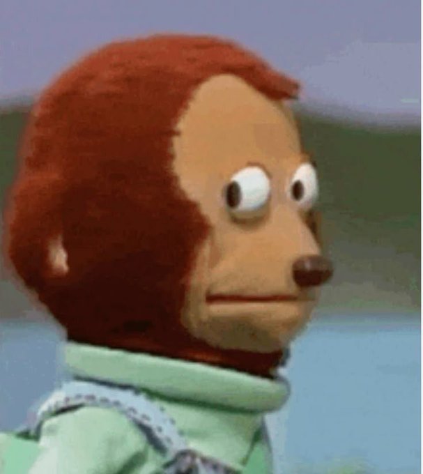A close-up of a puppet character with reddish-brown fur, a peach-colored face, large round eyes, a brown nose, and a neutral expression, wearing a light green shirt with white trim.