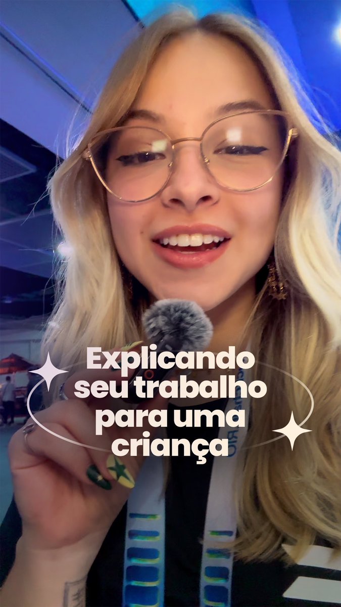 A blonde woman with glasses holds a microphone, with Portuguese text reading 'Explicando seu trabalho para uma criança' displayed prominently.