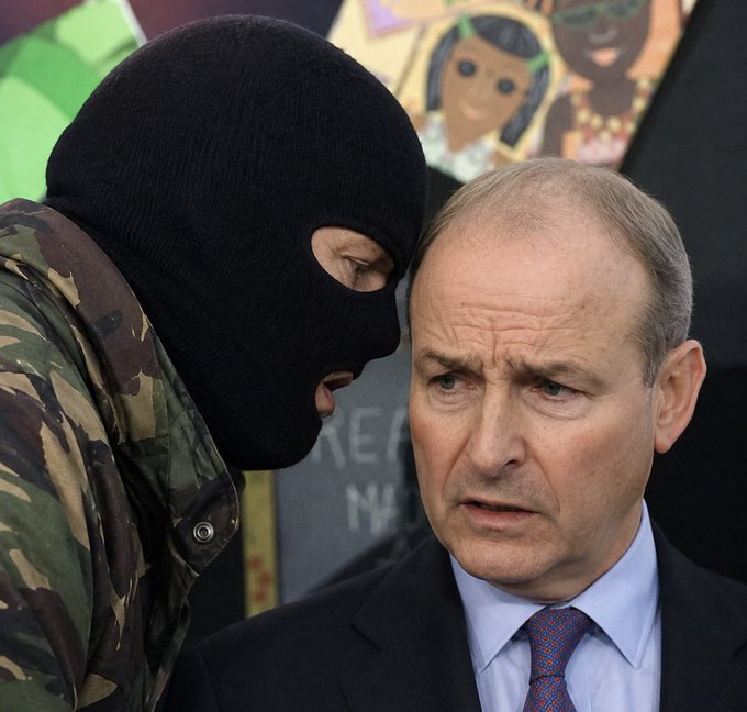 A masked figure in camouflage leans in to whisper urgently to a serious-looking suited man, with "REAL" partially visible on a sign behind them. The image humorously illustrates the post's joke, depicting the suited man (appearing to be a politician) being briefed that a "second IRA has been formed"—a tongue-in-cheek reference to fears of renewed paramilitary activity in Northern Ireland.