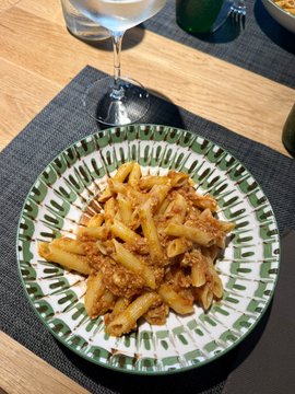 A plate of pasta with meat sauce is served on a green and white patterned dish at a restaurant table, accompanied by a glass of white wine. The image captures an Italian dining experience, fitting the post's mention of visiting Italy.