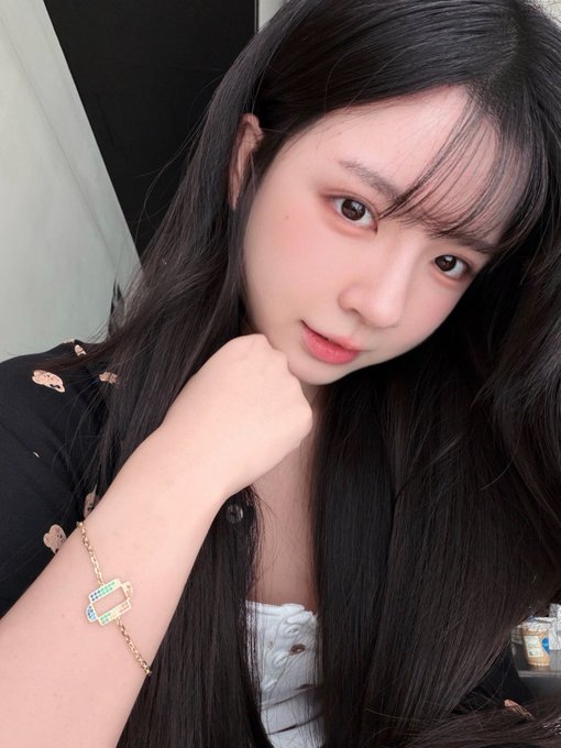 A selfie of a young woman with long dark hair wearing a black top with cutouts and a gold charm bracelet.