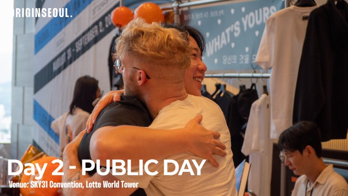 Two men share a hug at what appears to be a convention; overlaid text reads 'RIGINSEOUL.', 'Day 2 - PUBLIC DAY', and 'Venue: SKY31 Convention, Lotte World Tower.'
