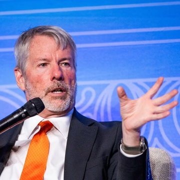 Michael Saylor, executive chairman of MicroStrategy, gestures while speaking at an event against a blue backdrop with ornate patterns. The image complements the post's theme of his long-standing Bitcoin conviction, visually representing the bold and outspoken stance that has defined his cryptocurrency advocacy.