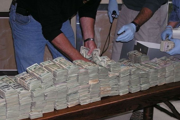 A large quantity of US dollar bills, primarily $20 and $100 denominations, are stacked on a table as individuals in blue gloves count and handle them. This illustrates the tangible nature of traditional currency, contrasting with the digital self-custody of Bitcoin mentioned in the post.