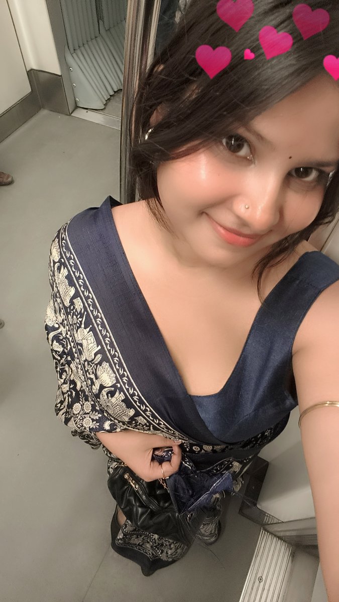 A selfie of a smiling woman with a nose stud wearing a blue and patterned dress, with pink heart filters overlaid on the image.