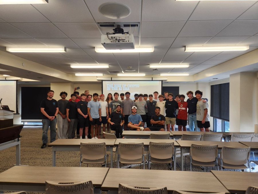 A large group of young men poses for a photo in a classroom, with a projection screen behind them displaying 'THE RISE OF CRYPTO IN THE AI ERA'.