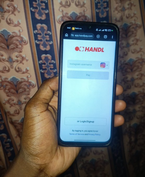 A hand holds a smartphone displaying the 'HANDL' payment app interface with an Instagram username field and a 'Pay' button.
