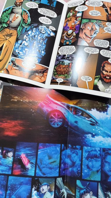 An open comic book displays colorful superhero-style panels with action scenes and dialogue, including a dramatic spread of a sleek car splashing through water.