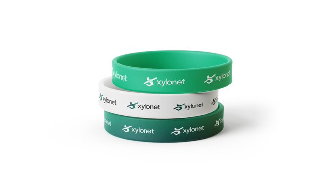 Three stacked silicone wristbands in light green, white, and dark green, each printed with the "xylonet" logo and name, promoting the Xylonet project's transition from testnet to mainnet readiness in collaboration with Arc on September 16th.