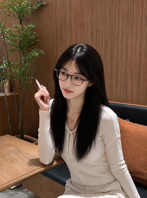 A young woman with long black hair and glasses poses in a cafe setting, wearing a white blouse and holding what appears to be a pen. The image doesn't show any visible text, numbers, or account names, but it appears to be a personal photo the user is sharing as part of their post celebrating a 10-year blue V renewal milestone and seeking followers.