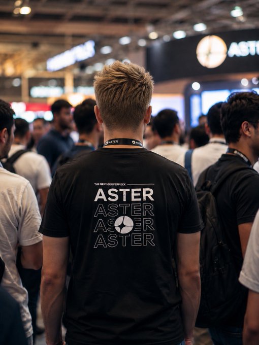 A photograph of a person from behind wearing a black 'ASTER' t-shirt with 'THE NEXT-GEN PERP DEX' text, standing in a crowded event venue with the Aster logo visible on signage.