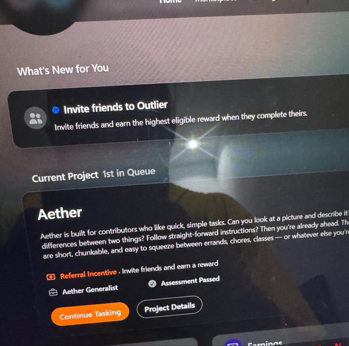 The image shows a computer screen displaying an invitation page from Outlier, which appears to be a project management tool or application. The text on the screen invites users to "Invite friends to Outlier". It also provides information about the current project status, stating that the project is in progress and has been completed by the user. Additionally, there are two options available for the user: they can either continue working on the project details or refer a friend who might be interested in joining the project. The image also includes a small orange button labeled "Continuous Tasking" at the bottom of the screen.