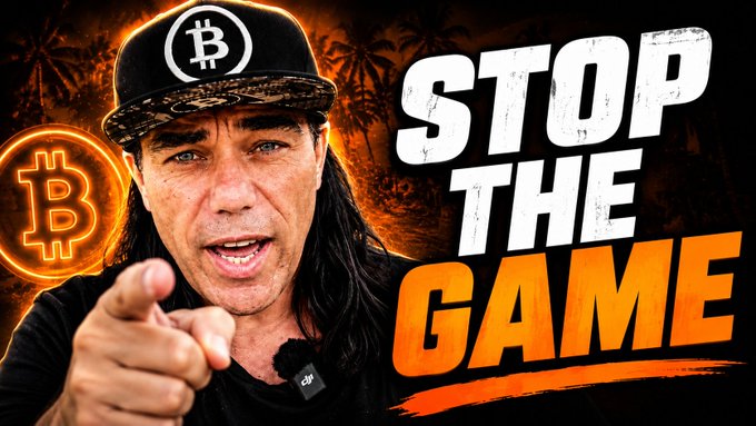 A man wearing a Bitcoin cap points at the camera beside bold "STOP THE GAME" text and a glowing Bitcoin logo, illustrating the video's message of escaping the traditional tax system rather than merely optimizing within it.