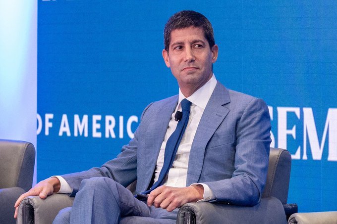 The image features a man dressed in a suit, sitting down with his hands clasped together. He appears to be at an event or gathering where he is seated next to a blue wall that displays the words "Focus on" and "Today's FOMC meeting will be chaired by the first-ever pro-Bitcoin chairman." The man seems to be engaged in conversation, possibly discussing the topic of Bitcoin as it relates to the Federal Reserve Chair.

The image also includes chairs placed around the room where people are seated, indicating that this is a social event or gathering.