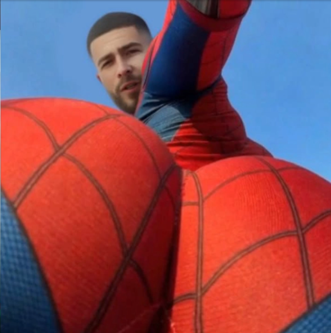The image shows a low-angle view of a person wearing a Spider-Man costume, with their face visible above the chest area, set against a blue sky. The caption humorously notes that AyeeZee (a Kick streamer) appears to be in the Spider-Man movie, playing on the actor's resemblance to the costumed figure in the viral clip.