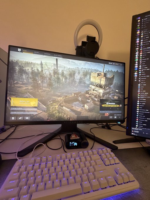 A gaming setup featuring a monitor displaying the main menu of 'Squad' with a 'DEPLOY TO NARVA' option, a white mechanical keyboard, and a vertical secondary monitor showing a chat or friend list.