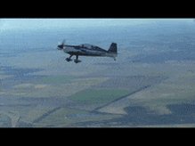 The image shows a small airplane flying high above a field, with its wings spread wide as it soars through the sky. Below the airplane, there are fields of land that extend into the distance. The text "SUIIIIIIIIII" is visible in the image and appears to be part of the caption provided by the post.